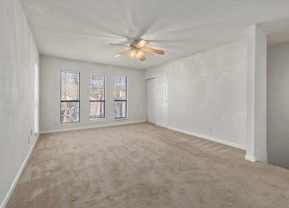 an empty living room with a ceiling fan and window