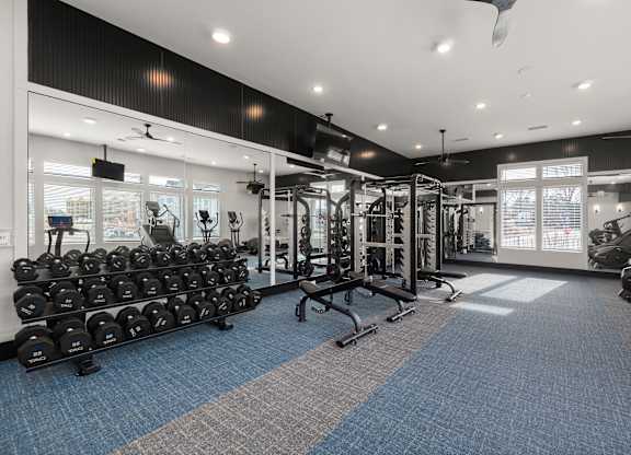 A gym with a variety of equipment including dumbbells, weight machines, and a bench.