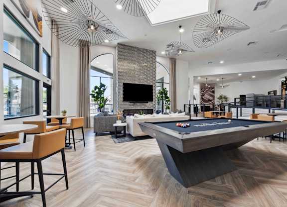 A pool table is in the middle of a room with a bar and a television.