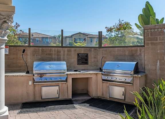 A stone wall with two built-in BBQ grills and a plaque on it.