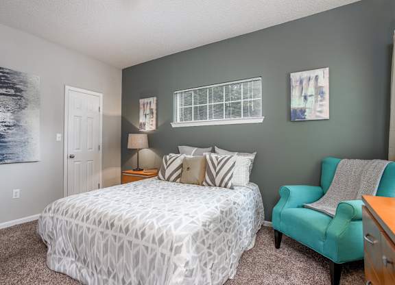 A bedroom with a bed, chair, and two pictures on the wall.