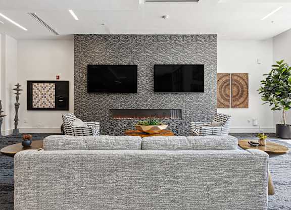 a living room with a gray couch and two televisions on the wall