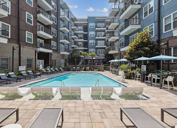 an outdoor swimming pool with lounge chairs and umbrellas in front of an apartment building