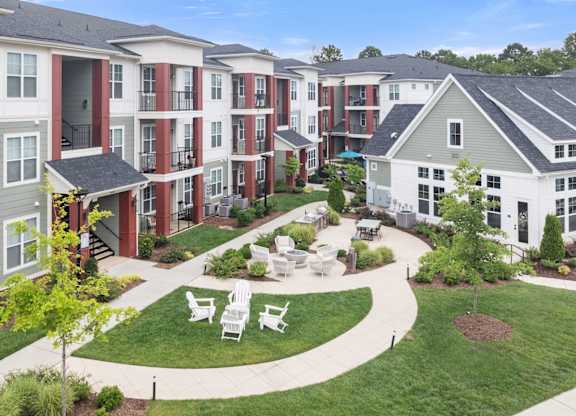 Apartment complex with a green lawn and white chairs.