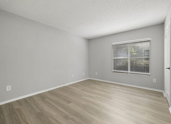the spacious living room of an apartment with a window and wooden floors