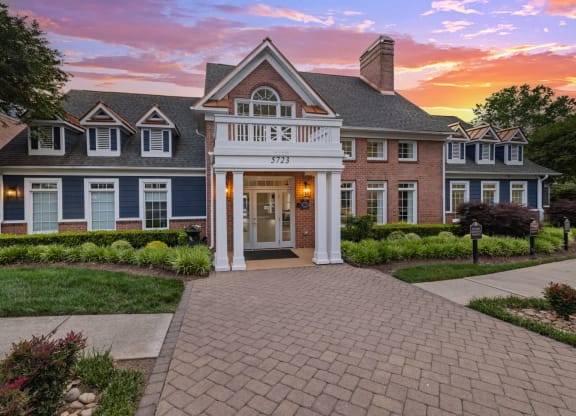a large house with a brick driveway and a sunset behind it