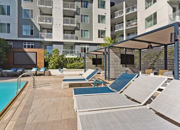 A pool area with sun loungers and a building in the background.