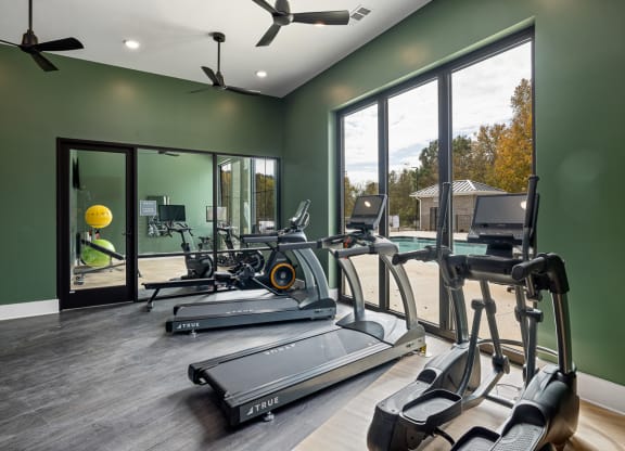 Fitness area with floor to ceiling windows looking out to the pool area. Treadmills, ellipticals and a yoga space with fans