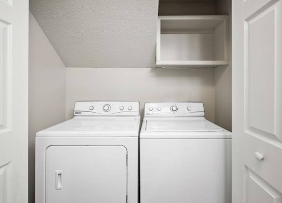Two white front loading washing machines in a small laundry room.