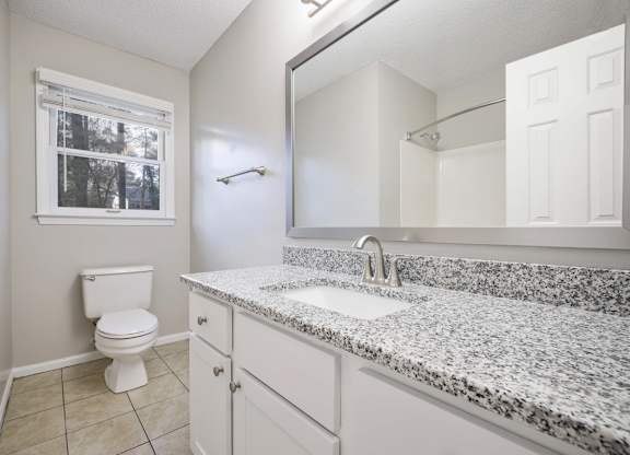 A bathroom with a granite counter top and white cabinets.