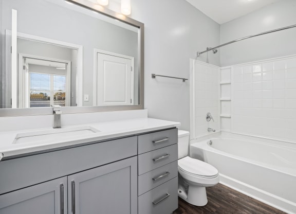 a bathroom with gray cabinets and a white bathtub