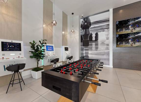 A foosball table is in the middle of a room with a wall of screens behind it.