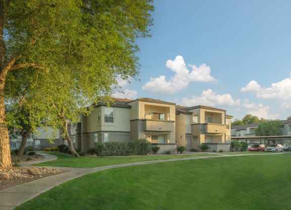 a row of apartment buildings with a green lawn and trees