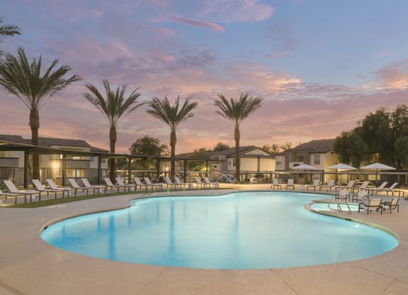 a swimming pool with chairs and palm trees at dusk