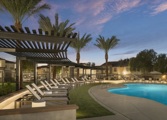 a swimming pool with chaise lounge chairs at night