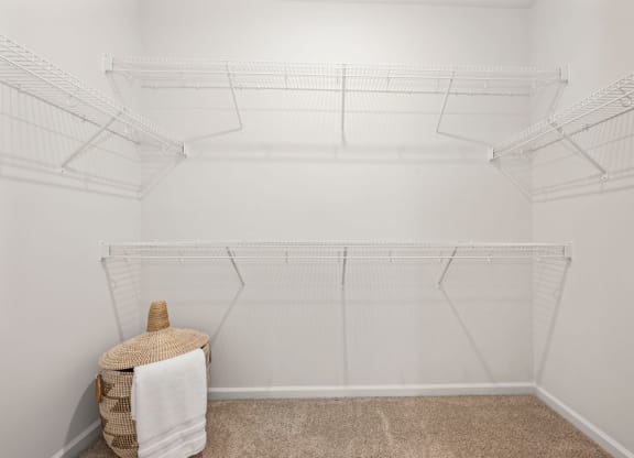 a walk in closet with white walls and shelves and a basket on the floor