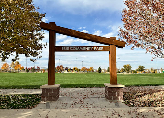 A wooden sign that says Erie Community Park stands in front of a field.