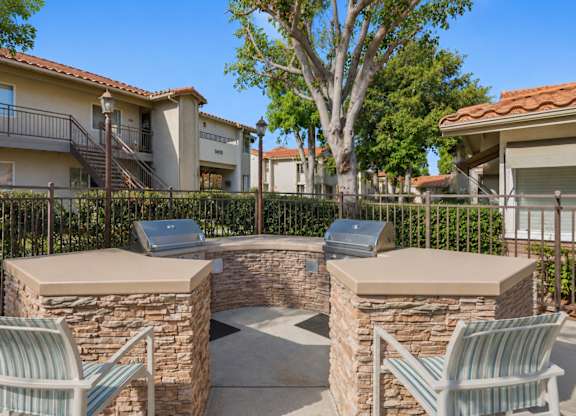 An outdoor grilling area with two grills and chairs.