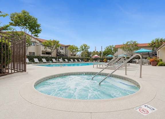 A relaxing spa next to a pool with lounge chairs and umbrellas.