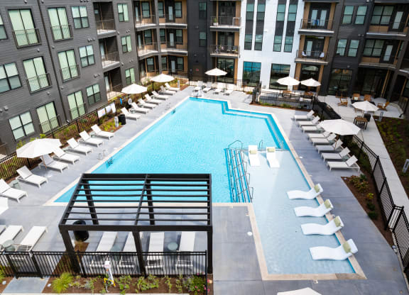 a swimming pool with lounge chairs and umbrellas at an apartment building