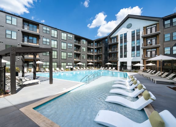 a swimming pool with white lounge chairs in front of an apartment building