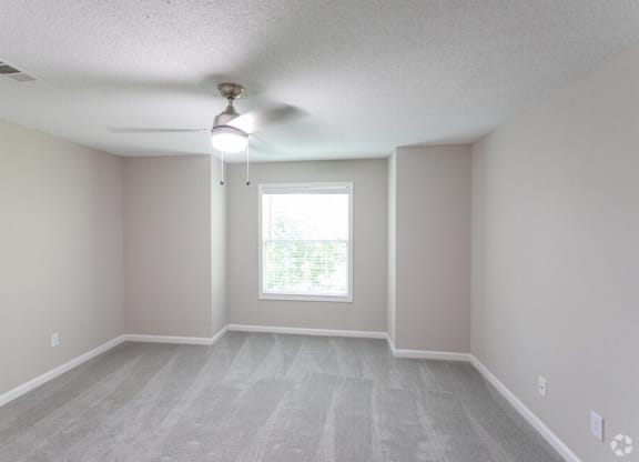 an empty living room with a ceiling fan and a window