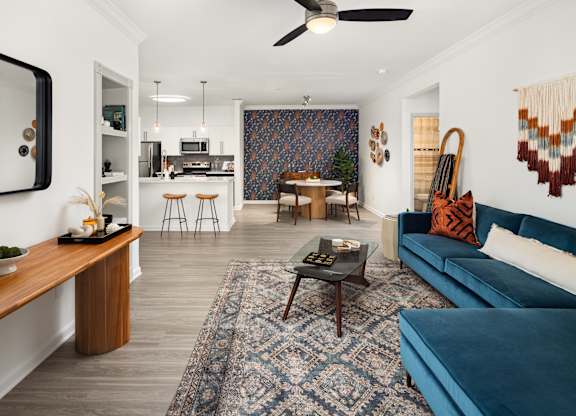a living room with a blue couch and a rug and a kitchen in the background