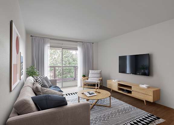 A living room with a grey couch, a wooden coffee table, a flat screen TV, and a large window with curtains.