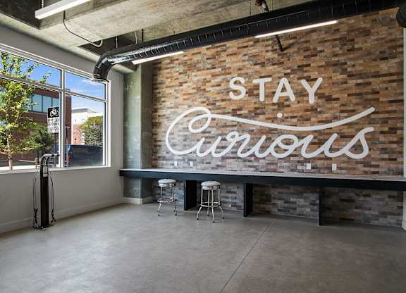 A room with a brick wall and a neon sign that says "Stay Curious".