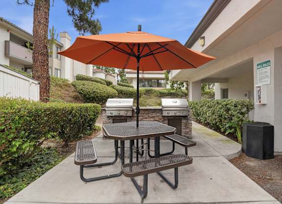 A picnic table with an orange umbrella is in the foreground of a building.