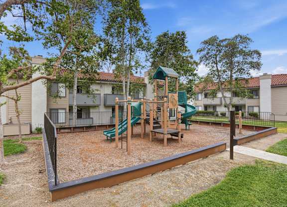 A playground with a slide, swings, and a seesaw in a residential area.