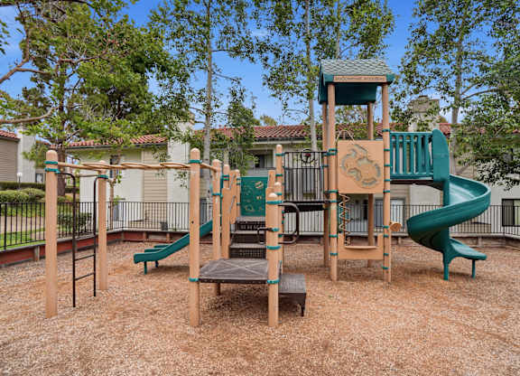 A playground with a green slide and a wooden structure.