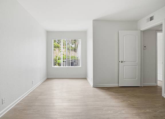 A room with a white door and a window with a view of trees.