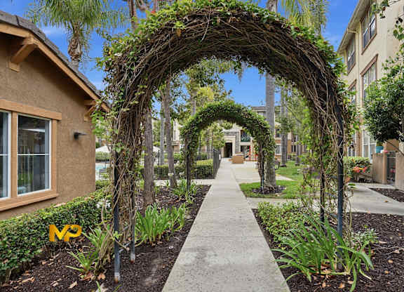 A garden pathway leads to a building with a trellis of vines.