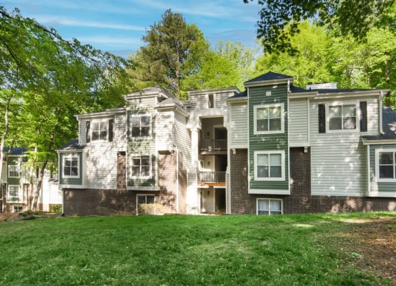 an apartment building with gray and green siding and a green lawn in front of it