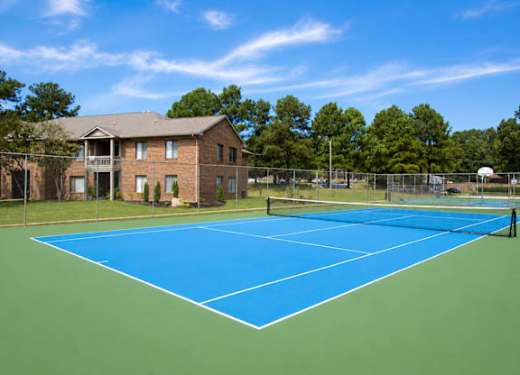A tennis court is surrounded by a fence and a brick building.