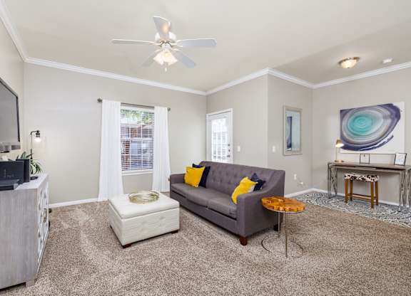 A living room with a grey couch, a television, and a ceiling fan at Clear Creek Meadows Apartments, Copperas Cove, Texas