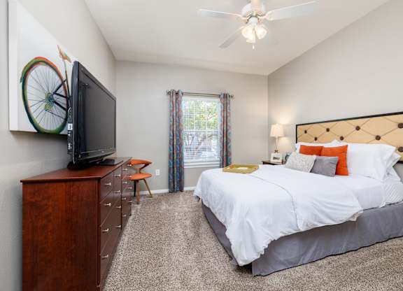 A bedroom with a bed, dresser, and television at Clear Creek Meadows Apartments, Copperas Cove