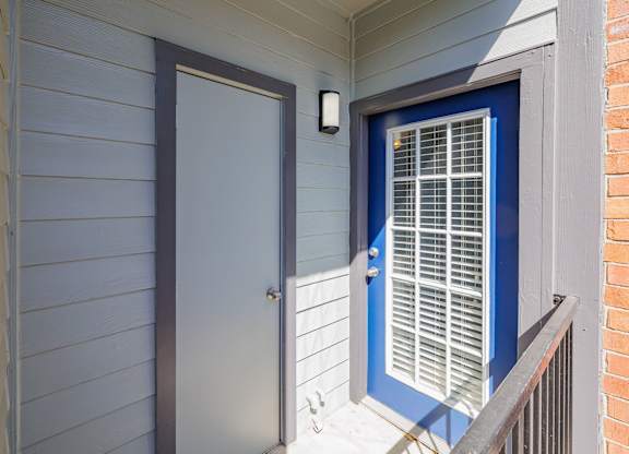 A blue door with a window is on the right side of a white wall at Clear Creek Meadows Apartments, Texas, 76522