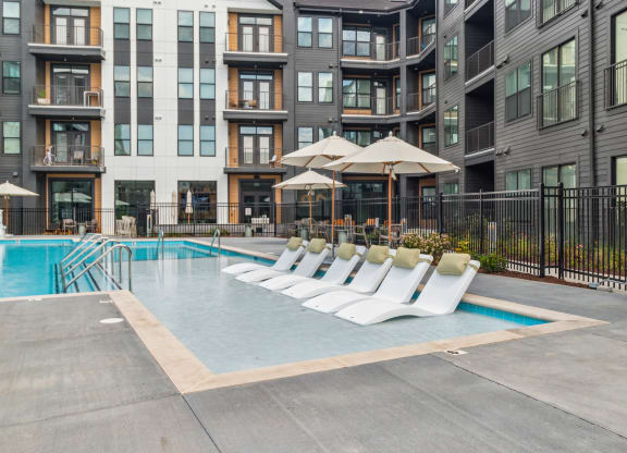 a pool with white lounge chairs in front of an apartment building