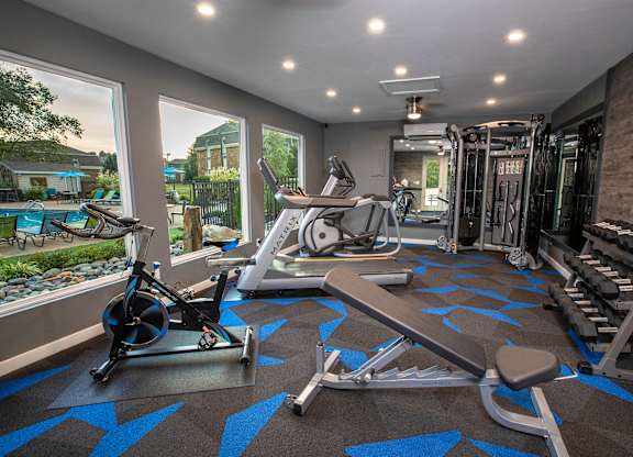 A home gym with a variety of equipment including a stationary bike, rowing machine, and weight rack.