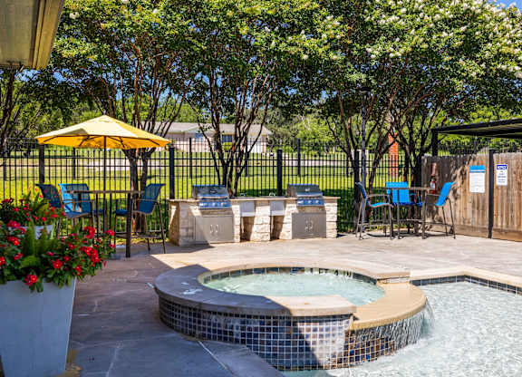 A small hot tub sits in the middle of a patio surrounded by chairs and a yellow umbrella at Clear Creek Meadows Apartments, Texas