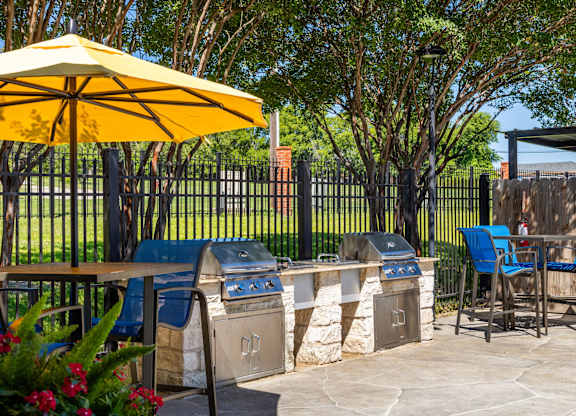A patio with a yellow umbrella, blue chairs, and a grill at Clear Creek Meadows Apartments, Copperas Cove
