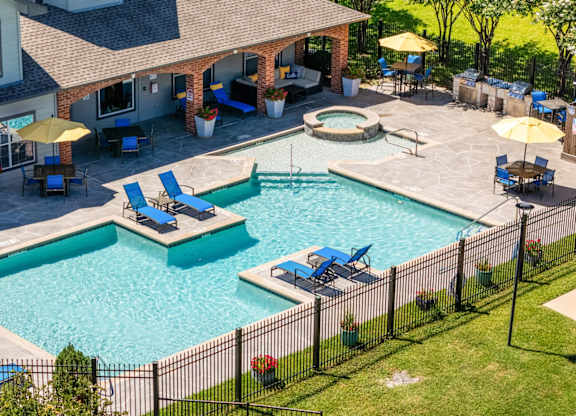 A pool surrounded by a black fence with blue lounge chairs and yellow umbrellas at Clear Creek Meadows Apartments, Apartments, Copperas Cove, TX
