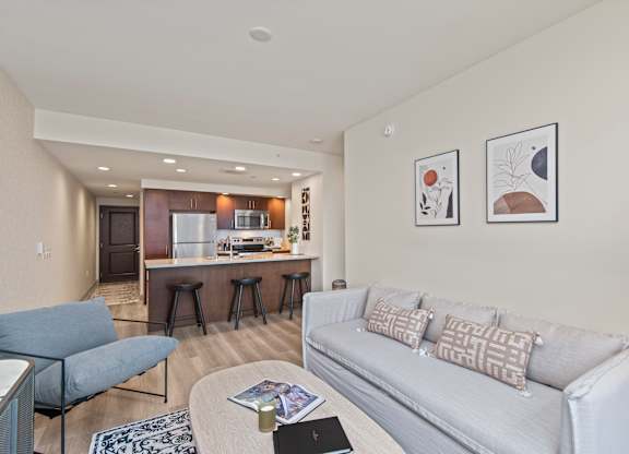 a living room with a couch a chair a table and a kitchen in the background