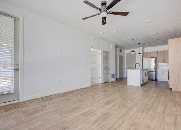 an empty living room and kitchen with a ceiling fan