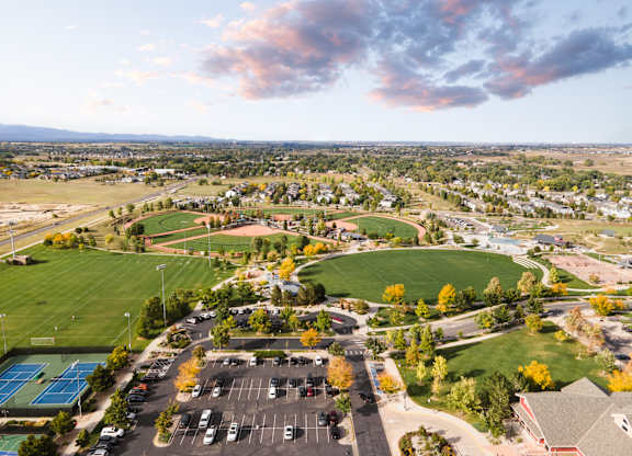 A park with a tennis court and a parking lot.