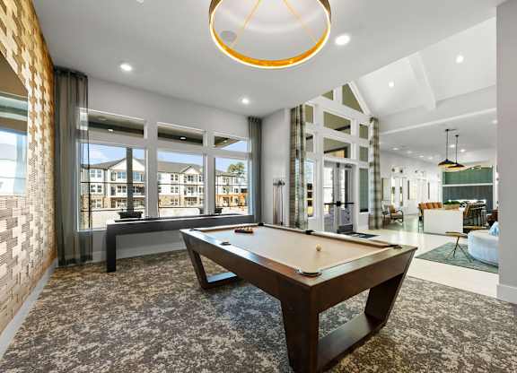 A pool table is in the middle of a room with a brick wall and a window.