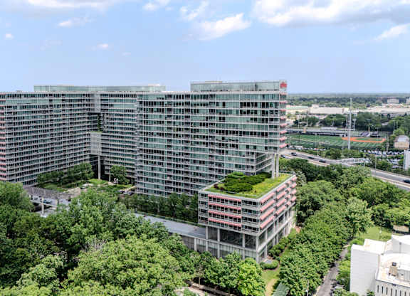 A large glass building with a green roof is surrounded by trees.