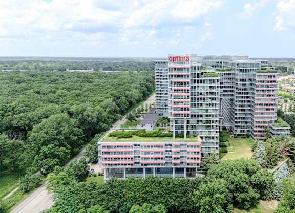 A tall building with the word "optima" on the side is surrounded by trees.